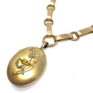 May include: A gold locket necklace with a detailed design of wheat stalks and a crescent moon with a star. The locket is adorned with small, clear rhinestones.