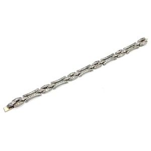 May include: A silver bracelet with a geometric design featuring rows of clear rhinestones.