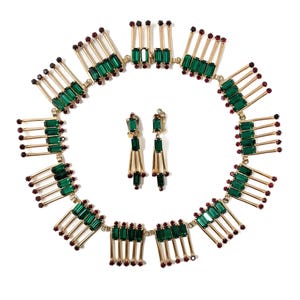 May include: A vintage jewelry set featuring a necklace and matching earrings. The necklace and earrings have a gold-tone metal base with emerald green rectangular stones and small red accents. The necklace is circular, and the earrings are dangling.
