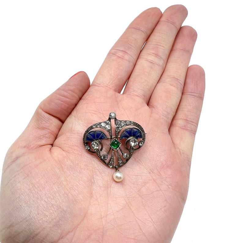 K&ouml;nnte beinhalten: Ein silberner Anh&auml;nger mit einem blauen und gr&uuml;nen Emaille-Design, besetzt mit Diamanten und einem Perlen-Tropfen.