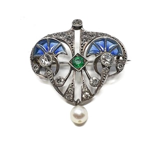 K&ouml;nnte beinhalten: Eine Brosche aus Silber und Emaille mit einem Perlenanh&auml;nger. Die Brosche zeigt ein stilisiertes Design mit blauem Emaille und einem gr&uuml;nen Edelstein.
