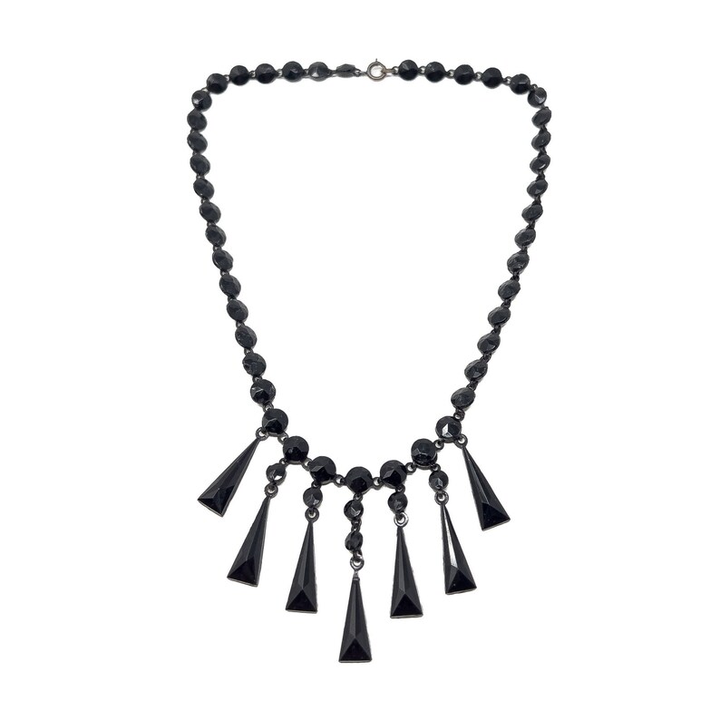 May include: A black necklace with a row of round beads and a dangling fringe of triangular beads.