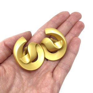 May include: A pair of gold-toned clip-on earrings with a twisted, abstract design.