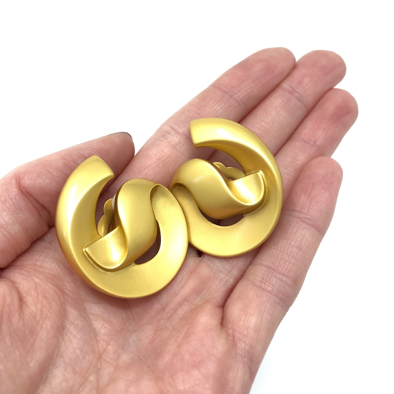 May include: A pair of gold-toned clip-on earrings with a twisted, abstract design.