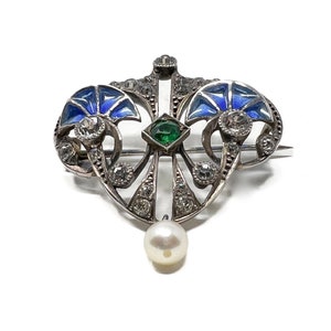K&ouml;nnte beinhalten: Eine silberne Brosche mit blauem Email, einem gr&uuml;nen Edelstein und einem Perlenanh&auml;nger. Die Brosche ist im Jugendstil gehalten.