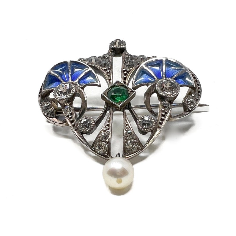 K&ouml;nnte beinhalten: Eine silberne Brosche mit blauem Email, einem gr&uuml;nen Edelstein und einem Perlenanh&auml;nger. Die Brosche ist im Jugendstil gehalten.