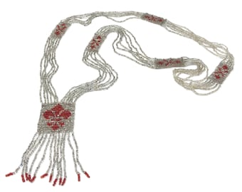May include: A long silver beaded necklace with red beaded accents. The necklace has a tassel at the bottom and is made of multiple strands of beads.
