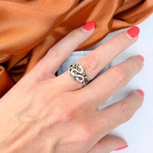 May include: A silver-toned metal ring featuring a detailed, coiled snake design that wraps around the band. The ring has a polished finish with visible texture along the serpent's body, showcasing a continuous, intertwined pattern across the finger.