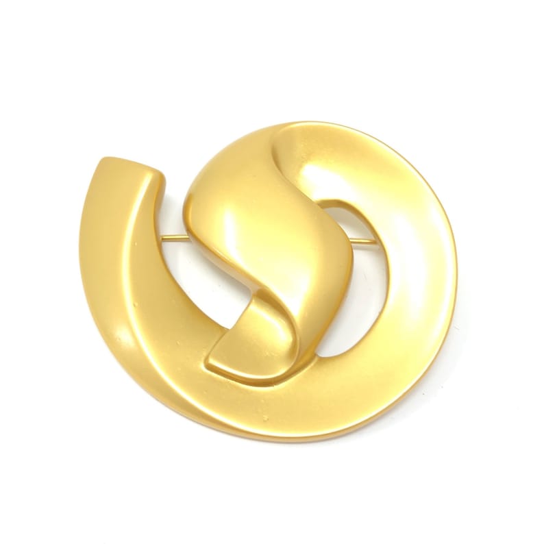 May include: A gold-toned brooch in the shape of an abstract swirl design.