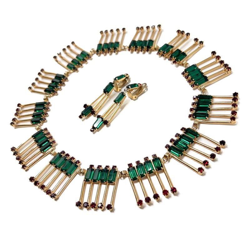 May include: A vintage jewelry set featuring a necklace and matching earrings. The necklace and earrings have a gold-tone metal base with emerald green and ruby red colored rhinestones. The necklace is a collar style.