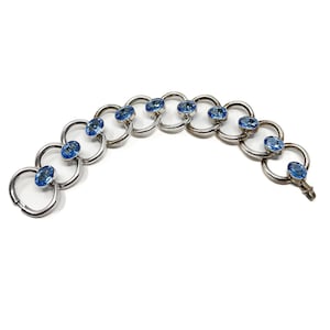 Puede incluir: Un brazalete de plata con un diseño de cadena de eslabones y detalles de cristal azul.
