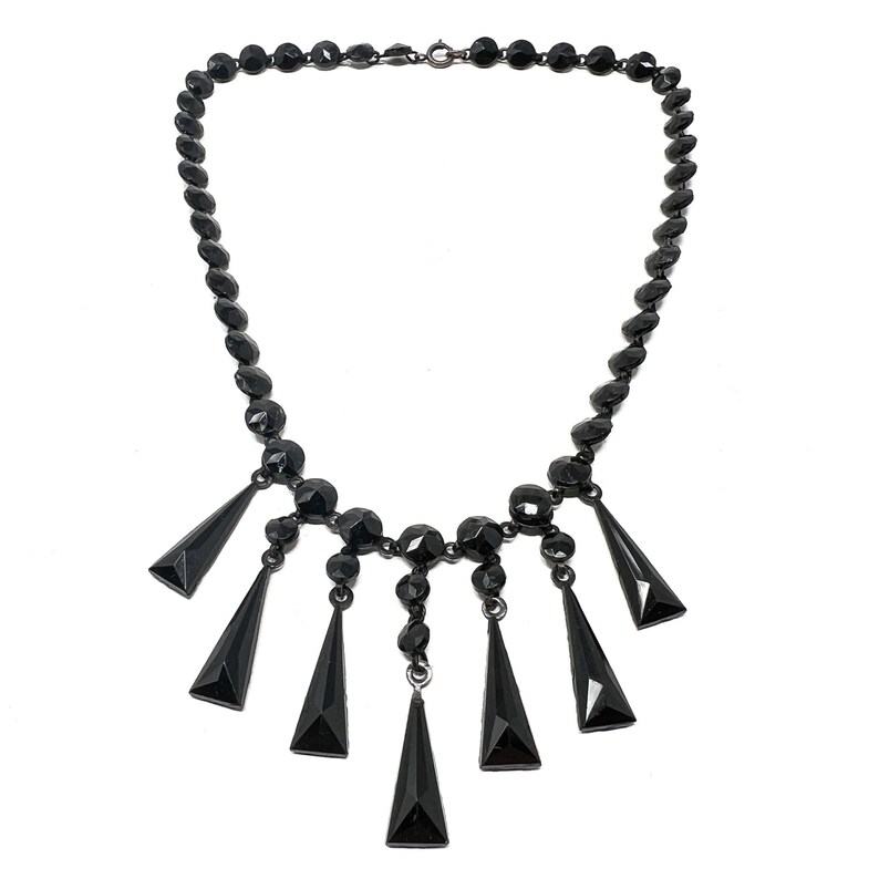 May include: A black glass necklace with a long chain and a dangling pendant of five black glass teardrop shapes.