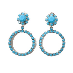 Puede incluir: Un par de pendientes colgantes de color azul turquesa con un diseño circular. Los pendientes están hechos de metal y tienen un grupo de piedras de color azul turquesa en la parte superior.