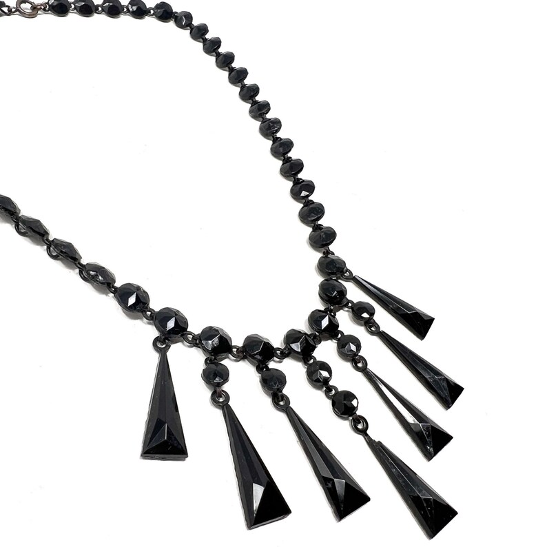 May include: A black beaded necklace with a dangling fringe of black faceted teardrop-shaped beads.