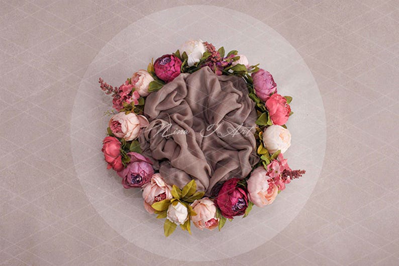 May include: A brown velvet fabric nestled in a circle of pink, white, and burgundy artificial flowers. The flowers are arranged in a wreath shape.