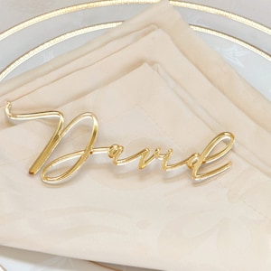 May include: Gold acrylic place card with the name "David" written in a cursive font.