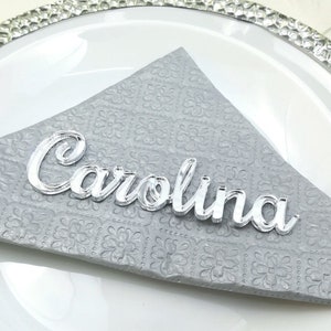May include: Silver acrylic name card with the name "Carolina" written in a cursive font.