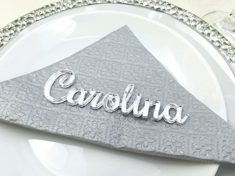 May include: Silver acrylic name card with the name "Carolina" written in a cursive font.