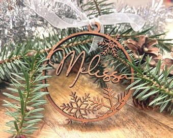 May include: A wooden Christmas bauble with the name "Melissa" cut out in the centre. The bauble is decorated with snowflake designs.