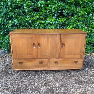 May include: A rectangular wooden sideboard featuring three vertical cabinet doors across the top section and two wide horizontal drawers positioned below. The furniture piece is crafted from light brown wood with a visible grain and integrated handles.