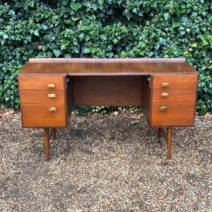 May include: A rectangular wooden desk featuring a smooth top surface and a total of six drawers, with three drawers on each side. Each drawer is equipped with a small, rectangular brass-coloured handle. The desk is supported by four tapered legs.