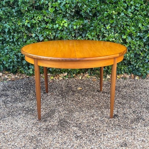 May include: A round wooden dining table with a smooth, light brown finish and a visible wood grain pattern. The table features a circular top with a central seam and four tapered, cylindrical legs that extend outward from the base.