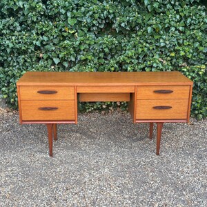 May include: A rectangular wooden desk featuring a light brown finish with four drawers, two on each side. Each drawer is equipped with a dark brown, oval-shaped handle. The desk is supported by four tapered wooden legs, providing a stable base.