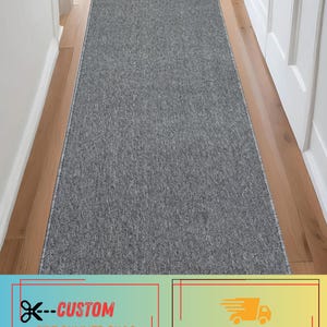 May include: A long, rectangular runner rug featuring a solid, textured charcoal gray surface with a fine, heathered pattern. The rug has clean, finished edges and is positioned lengthwise, covering the center of a narrow indoor hallway floor.