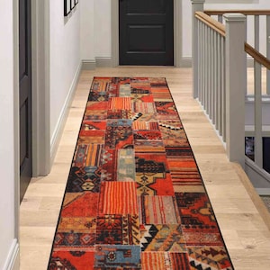 May include: A red, orange, and blue patterned runner rug with a patchwork design. The rug is laid out on a wooden floor in a hallway.