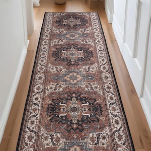 May include: A long, rectangular area rug with an ornate, traditional design. The rug features a central pattern in shades of rust, black, and blue, framed by a cream-colored border. The rug is placed on a hardwood floor.