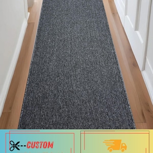 May include: A long, rectangular runner rug featuring a textured, heathered dark gray and black surface. The rug has a low-profile pile with a consistent, speckled appearance throughout, finished with a clean, bound edge along the entire perimeter.