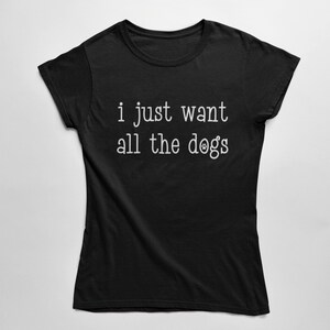 May include: Black t-shirt with the white text "i just want all the dogs". The text includes a paw print in place of the letter "o" in "dogs". The shirt is made of a soft material and has short sleeves.