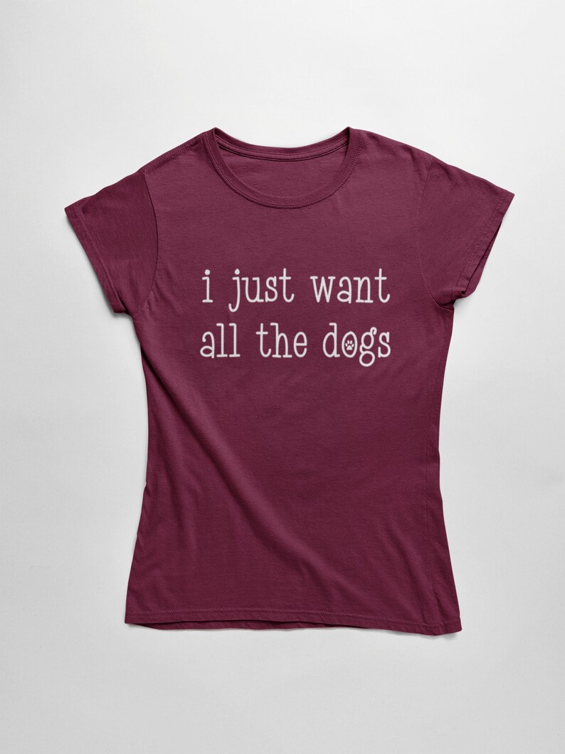 May include: Burgundy t-shirt with the text "i just want all the dogs" in white. The word "dogs" has a paw print graphic. The shirt is a crew neck and has short sleeves.
