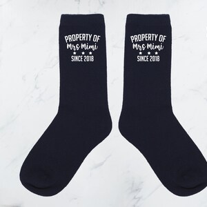 May include: Pair of navy blue socks with white text that reads "PROPERTY OF Mrs Mimi SINCE 2018".