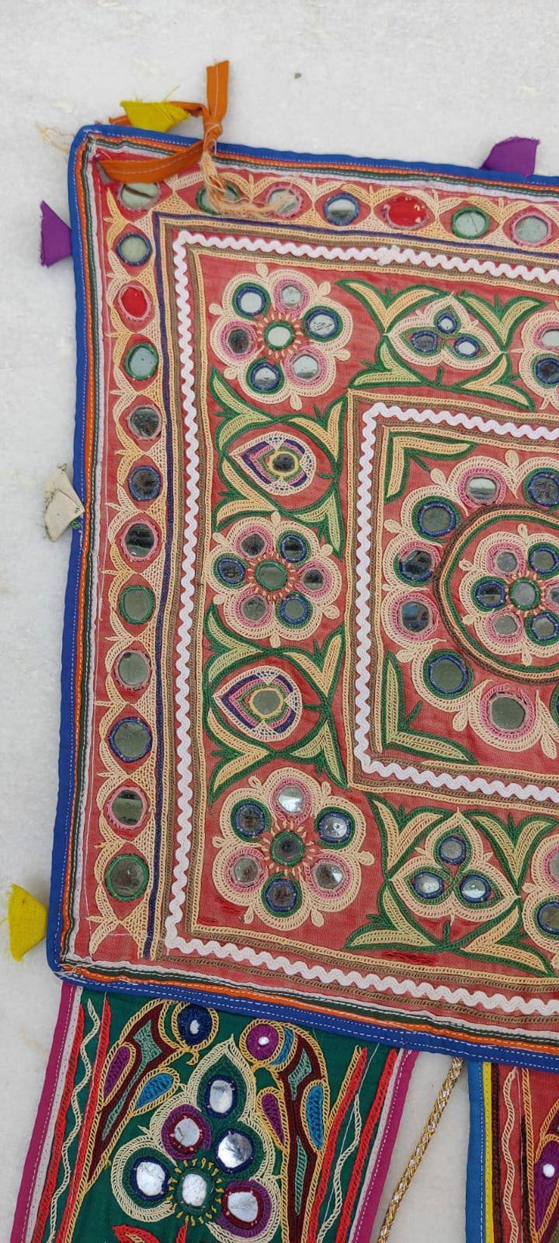 Puede incluir: Un tapiz de pared textil colorido con bordados intrincados y adornos de espejo. El dise&ntilde;o presenta motivos florales y patrones geom&eacute;tricos en tonos rojos, verdes, azules y amarillos.