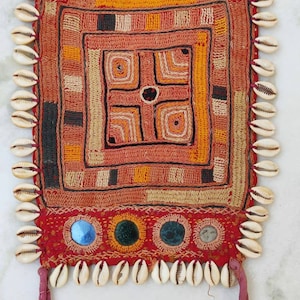 Könnte beinhalten: Eine rote, orange und braune gehäkelte Stofftasche mit geometrischem Muster und kleinen runden Spiegeln. Die Tasche ist mit einem Fransenbesatz aus weißen Muscheln verziert.