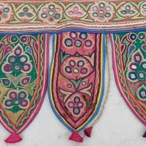 Puede incluir: Una guirnalda de tela colorida con borlas, con dise&ntilde;os florales bordados y detalles de espejo. La guirlande est&aacute; hecha de algod&oacute;n y es perfecta para agregar un toque de estilo bohemio a la decoraci&oacute;n de tu hogar.