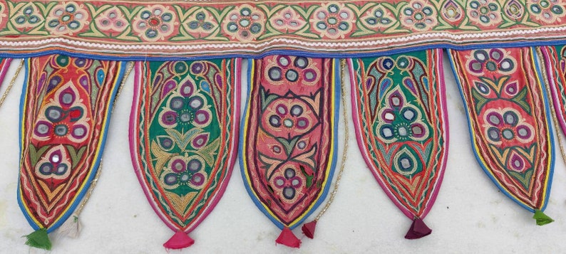 Puede incluir: Una guirnalda de tela colorida con borlas, con dise&ntilde;os florales bordados y detalles de espejo. La guirlande est&aacute; hecha de algod&oacute;n y es perfecta para agregar un toque de estilo bohemio a la decoraci&oacute;n de tu hogar.