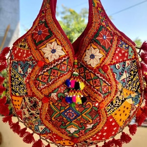 Puede incluir: Un bolso tote rojo, multicolor, bordado con borlas. El bolso está hecho de tela de patchwork y tiene una variedad de diseños florales y geométricos.