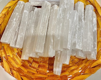 May include: A wicker basket filled with selenite crystal wands. The wands are white and have a striated texture. The text on the card reads: "Selenite is powerful enough to clear negative energies, and reprogram your crystals. You never need to recharge it! It can help in expanding your awareness and contacting your Spiritual Guides and Angels. Rubbing the stone may help you enter in the realm of dreams, intuition and in a meditative state. Selenite can be placed on the Third Eye Chakra to increase telepathic abilities. The insight it provides is valuable in any healing treatment."
