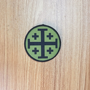 May include: A green and black embroidered patch with a cross in a circle. The cross has four smaller crosses on each arm.