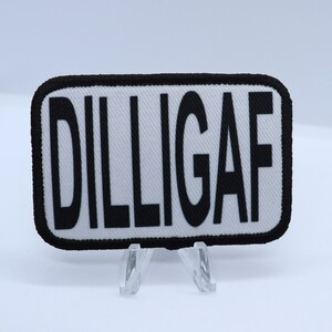 May include: White rectangular patch with black embroidered text that reads "DILLIGAF".