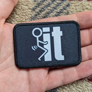 May include: A black patch with white stitching around the edges. The patch features a white stick figure flipping the bird with the word "it" next to it.