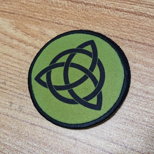 Peut inclure: Un patch brodé vert et noir avec un motif de nœud celtique. Le nœud est un symbole traditionnel d'interconnexion et d'éternité.