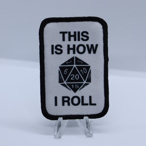 May include: White fabric patch with black text and a black and white image of a twenty-sided die. The text reads "This is how I roll."