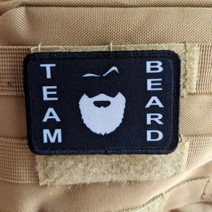May include: Black patch with white text that reads "TEAM BEARD" with a white cartoon beard and moustache in the centre.