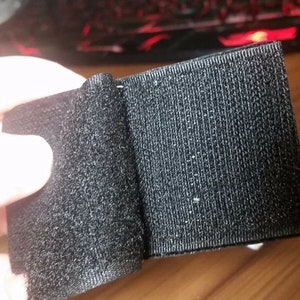 Peut inclure: Ruban adh&eacute;sif noir &agrave; crochets et boucles, &eacute;galement connu sous le nom de Velcro, pr&eacute;sent&eacute; pli&eacute; en deux. Le ruban est fait d'un tissu doux et textur&eacute;.