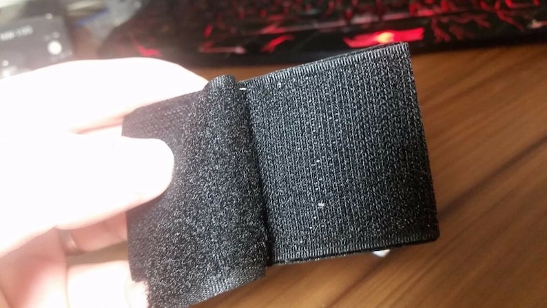 Peut inclure: Ruban adh&eacute;sif noir &agrave; crochets et boucles, &eacute;galement connu sous le nom de Velcro, pr&eacute;sent&eacute; pli&eacute; en deux. Le ruban est fait d'un tissu doux et textur&eacute;.