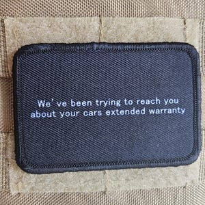May include: A black rectangular patch with white text that reads, "We've been trying to reach you about your cars extended warranty." The patch is sewn onto a tan fabric background.