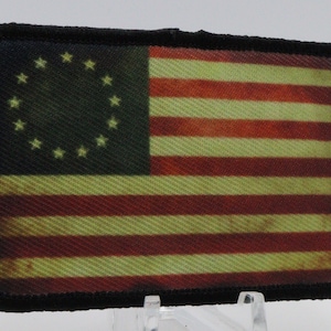 May include: A vintage-style American flag patch with 13 stars in a circle, sewn onto a black fabric backing.